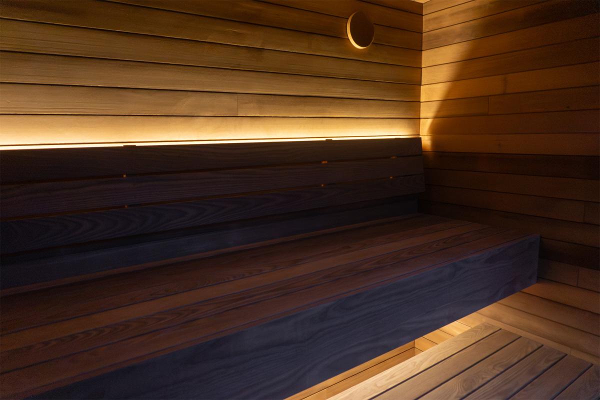 Wood benches and backrest with concealed lighting and a round wall vent inside the Ember Cabin sauna.