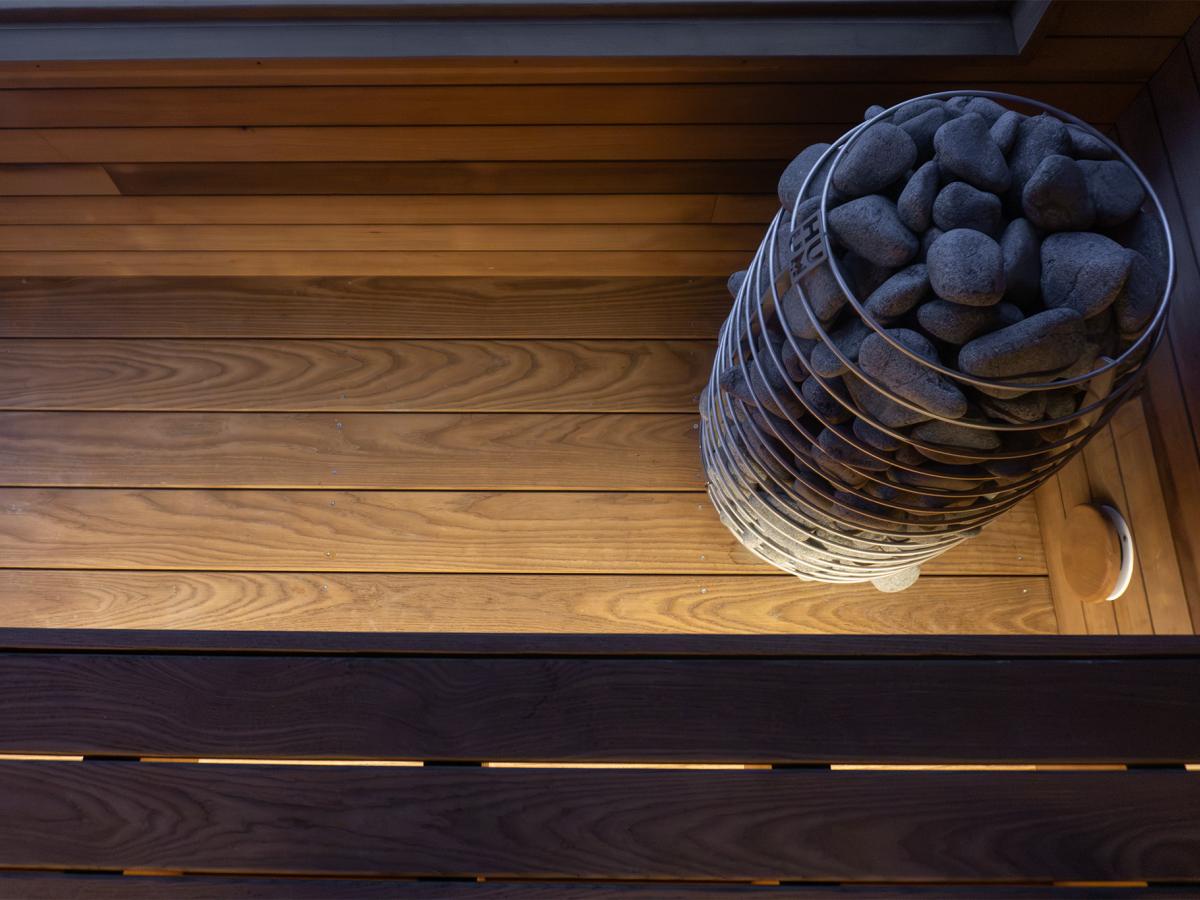 HUUM electric sauna heater beside wood flooring and a round wall vent inside the Ember Cabin